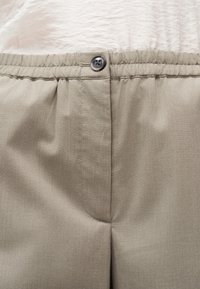 Μπεζ παντελόνι με ελαστική μέση και μαύρο κουμπί κλεισίματος, φορεμένο με λευκό τοπ από υφαντό ύφασμα.