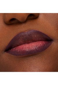 Syvä purppura ja ruusunvärinen huuliväri matta-finishillä, joka näyttää tekstuurity yksityiskohtia ja määritellyn huulirajan, lämpimän ihonsävyn taustalla.
