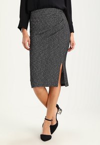 Jupe crayon noire et blanche à motifs, longueur genou, avec une fente sur le côté, fabriquée en tissu texturé, offrant un design ajusté et une taille élastique.