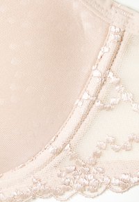 Beige lace bra cup featuring smooth fabric with delicate floral embroidery along the edge. Soft texture, lightly textured center panel.