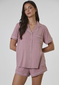 Rosa pyjamas-set med kort ärm i mjukt tyg, med en knäppskjorta som har ficka och kontrasterande vit passpoal på kragen och shorts.