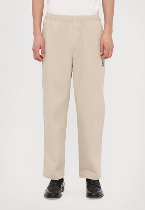 Beige elastic-waist trousers made of lightweight fabric. Features a straight cut and a side pocket with a blue logo detail.