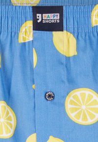 Blauwe shorts met een citroenpatroon, voorzien van een knoopsluiting en een elastische tailleband genaamd "HAPPY SHORTS." Lichte stof met een gladde textuur.