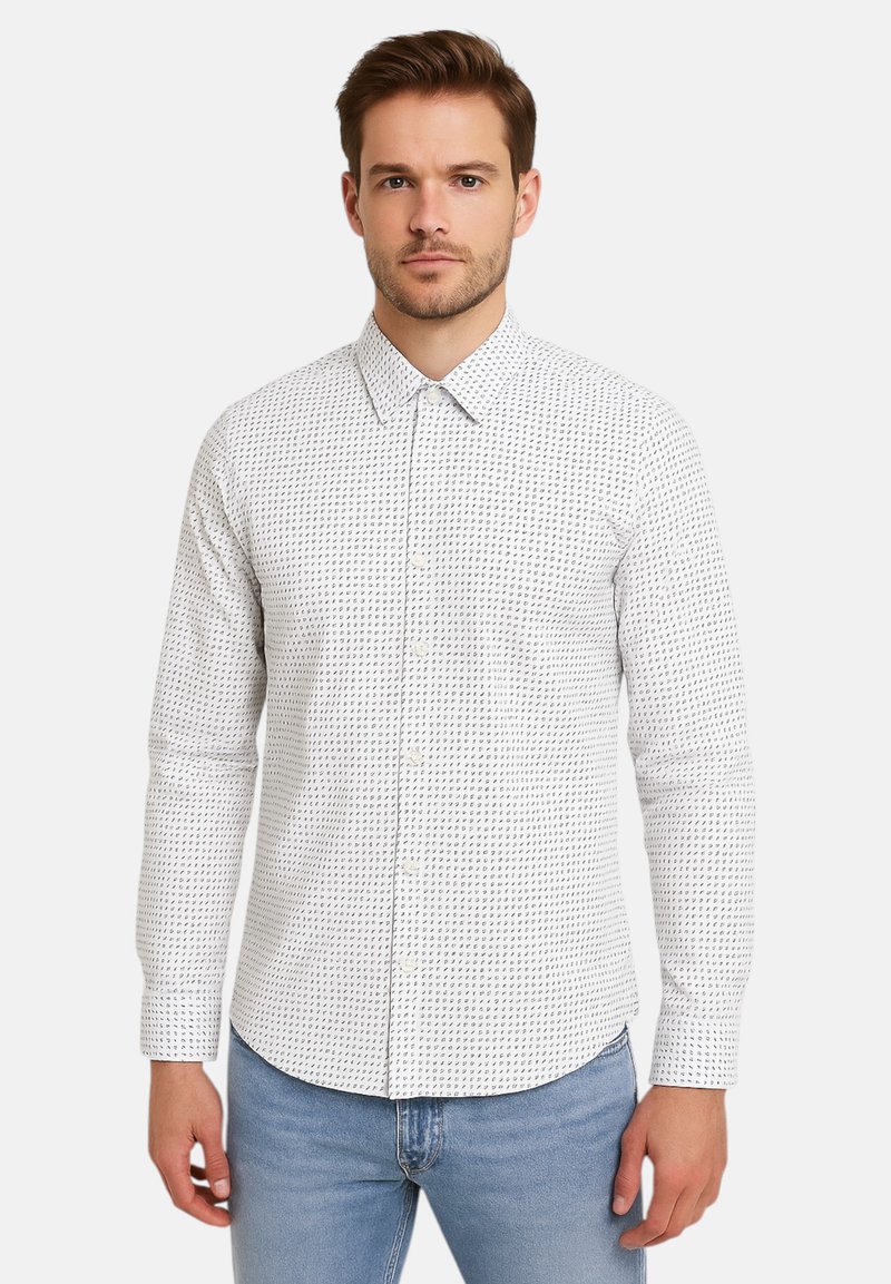 Camicia bianca con un motivo geometrico nero, maniche lunghe, colletto tradizionale e tessuto morbido, abbinata a jeans azzurri chiari.
