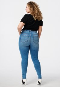 Hoggewaisted blauwe spijkerbroek met een soepele textuur, elastische tailleband en twee achterzakken. Gekleed met een zwart T-shirt met korte mouwen.