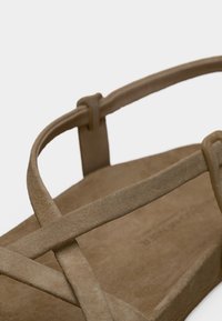 Ταμπά σανδάλι με λείο, σουέντ υλικό, λουριά που διασταυρώνονται και επίπεδη σόλα με ελάχιστη υφή.