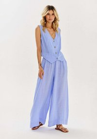 Svetlomodrý overal bez rukávov s výstrihom do V a detailom na gombíku, s voľnými nohavicami a uvoľneným strihom. Hladká, jemná tkanina.