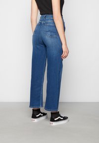 Jeans blu a vita alta con gambe larghe, realizzati in denim. Presentano due tasche posteriori e cuciture sottili. Abbinati a sneakers nere alte.