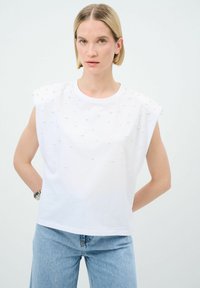 Vit bomullstopp med kort ärm och upphöjda pärlliknande detaljer. Avslappnad passform och rundad halsringning. Bärs tillsammans med ljusblå denimjeans.
