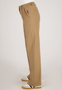 Beige rechte broek gemaakt van een soepele stof, met een elastische tailleband en zijzakken. G gedragen met witte en grijze schoenen.