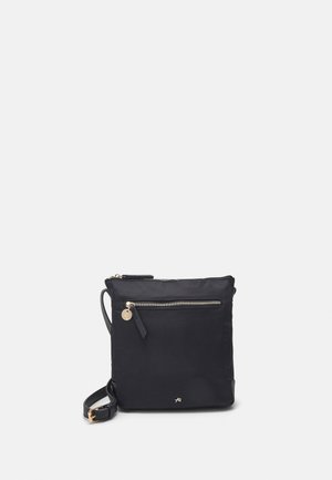 Zwarte vierkante crossbodytas met voorvak met rits, goudkleurige ritssluiting en verstelbare riem op een effen lichtgrijze achtergrond.