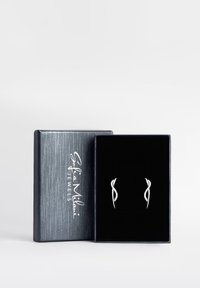 Srebrne kolczyki o falistym wzorze, ozdobione małymi diamentami, wyeksponowane w szarej, teksturowanej pudełku wyłożonym czarnym aksamitem.