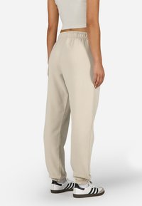 Bežové tepláky vyrobené z jemného materiálu, s elastickým pásom a manžetami, s uvoľneným strihom a minimalistickým dizajnom.