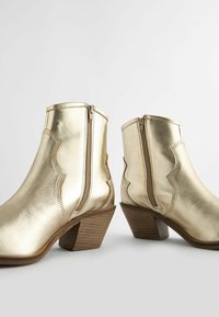 Botas metálicas doradas hasta el tobillo con un acabado de cuero texturizado, que cuentan con cremalleras laterales, un diseño curvado y un tacón apilado y cónico.
