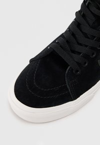 Czarne zamszowe sneakersy z gładką cholewką, okrągłym noskiem i białą gumową podeszwą. Czarne sznurówki i subtelne detale w postaci przeszyć podkreślają design.