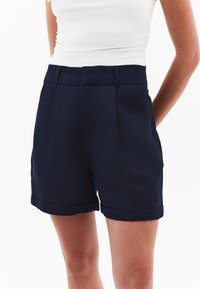 Námořnické modré šortky vyrobené z lehké látky, s vysokým pasem, záhyby a ohrnutými manžetami pro elegantní vzhled. Minimalistický design.