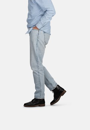 Lichtblauwe denim jeans met een slim fit, gecombineerd met zwarte leren veterschoenen. Het shirt is een lichtblauwe lange mouw met knopen.