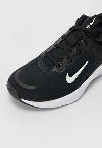 Black athletic shoe with a textured fabric upper, white swoosh logo, and black laces. Features a cushioned white midsole and rounded toe.