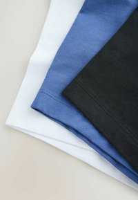 Tissu en coton blanc, bleu et noir plié et empilé sur une surface claire, montrant le détail de la couture de l'ourlet.