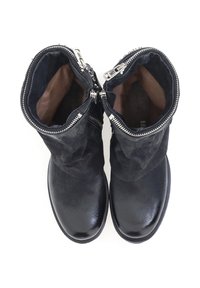 Botas de cuero negro hasta el tobillo con un diseño holgado, que presentan dos cremalleras plateadas y una textura suave. Interior forrado con tela marrón.