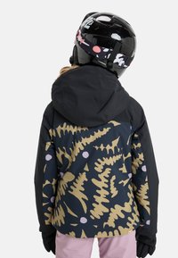 Schwarze Kapuzenjacke mit einem mehrfarbigen Farbmuster aus goldenen und rosa Farnen, getragen mit rosa Hosen und Handschuhen sowie einem schwarzen Helm.