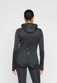 Zwarte sportjack met capuchon, gestructureerde zijkanten en een slim fit. Gladde stof met contrasterende materialen en een klein accentdetail aan de achterkant.