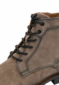 Bottine en suede taupe à lacets, avec des lacets ronds noirs, des œillets en métal et des détails cousus sur le côté et la zone des orteils.