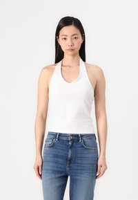 Bijela halter-top majica od mekanog materijala s v-izrezom. Uparena s pripijenim plavim trapericama koje prikazuju blago izbljedjivanje.