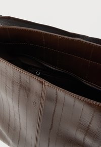 Borsa shopper in pelle marrone con superficie a strisce testurizzate; l'interno presenta una tasca con cerniera e una fodera liscia. Apertura superiore per un facile accesso.