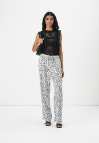 Top in pizzo nero con bordi scallop su pantaloni bianchi con una stampa astratta nera. Accessoriato con una piccola borsa nera e sandali.