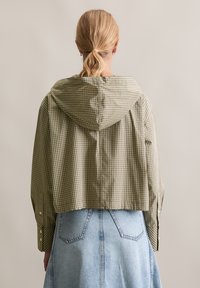 Gekürzte Kapuzenjacke im grün-cream karierten Muster. Sie verfügt über lange Ärmel mit geknöpften Bündchen und einen locker geschnittenen Schnitt.