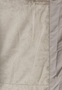 Krupan plan svjetlosmeđeg antilopa materijala s vidljivim šavovima i uskim trakama glatkog materijala s desne strane.