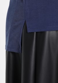 Námořnická modrá bavlněná trička s bočními rozparky, zkombinované s černou sukní z faux kůže. Texturovaná tkanina nabízí hladký vzhled.