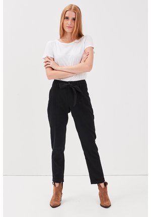 Pantalons noirs ceinturés avec une coupe décontractée, associés à un t-shirt blanc uni à manches courtes. Des bottines beige mettent en valeur la tenue.