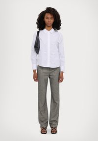 White shirt with 3D bow accents, gray textured trousers, and strappy black sandals. Model holds a small black shoulder bag.