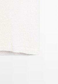 Strik en hvid sweater med ribkant og glat tekstur. Designet er enkelt uden mønstre eller yderligere accenter synlige.