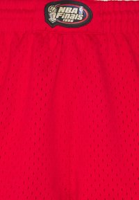 Pantalones cortos de baloncesto rojos hechos de tela de malla transpirable, con un parche bordado negro de la NBA Finals 1996 cerca de la cintura.