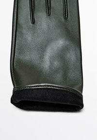 Guanto in pelle verde con tre linee cucite sul retro, dotato di un interno morbido nero al polsino per maggiore comfort.