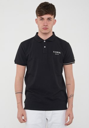 Schwarzes Polohemd aus Baumwolle mit klassischem Kragen, einer Knopfleiste mit zwei Knöpfen und weißem gesticktem Logo auf der linken Brust. Kurze Ärmel.