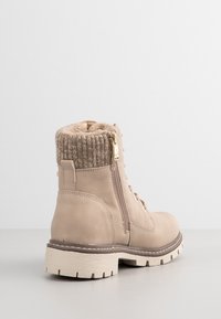 Bottine beige en daim avec bordure en maille, fermeture éclair latérale, devant lacé et semelle épaisse à crampons sur un fond neutre.