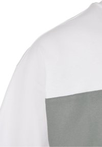 Kortsleeved t-skjorte med en hvit øvre seksjon og en grå nedre seksjon, med en myk tekstur og en sydd kant.