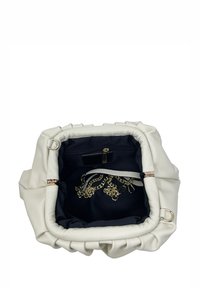 Krémová kabelka z faux kůže se shromážděným vrškem, černým textilním interiérem, zlatými řetězovými akcenty a vnitřními zipovými kapsami na jedné straně.