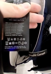 Étiquette de soin noire avec des instructions de lavage, des détails sur le tissu et des symboles d'entretien. Matériau : 100 % polyester, inclut le texte "Vêtement Durable".