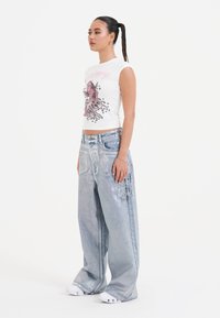 Hvid ærmeløs top med pink grafisk design, parret med oversized lyseblå denim jeans med broderede detaljer.