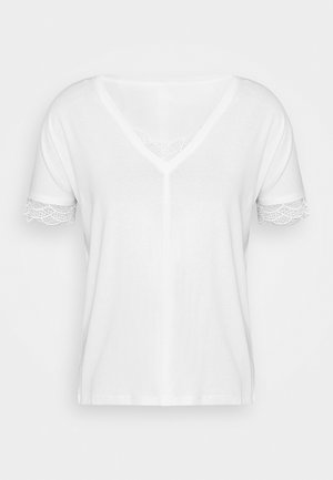 Chemise blanche à manches courtes avec col en V et bordure en dentelle aux manches et au col, présentée sur un fond clair uni.