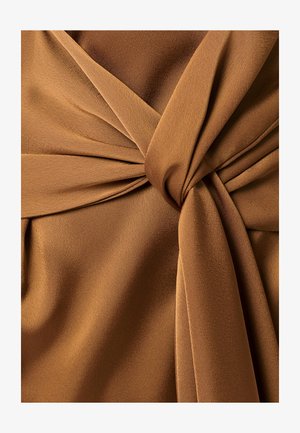 Zachte bruine stof strak gedraaid in een knoop, met zachte plooien en textuurvariaties in warm licht.