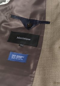 Beżowe wnętrze garnituru z brązową satynową podszewką, z czarną metką "Matinique", guzikiem oraz niebieską metką "Washable Suiting".