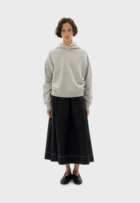 Sudadera gris con capucha y corte relajado, combinada con una falda larga negra con dobladillo simple y calzado negro.