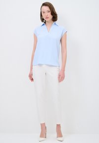 Blusa azzurra a maniche corte con colletto, abbinata a pantaloni bianchi slim-fit e scarpe con tacco beige. Design semplice.