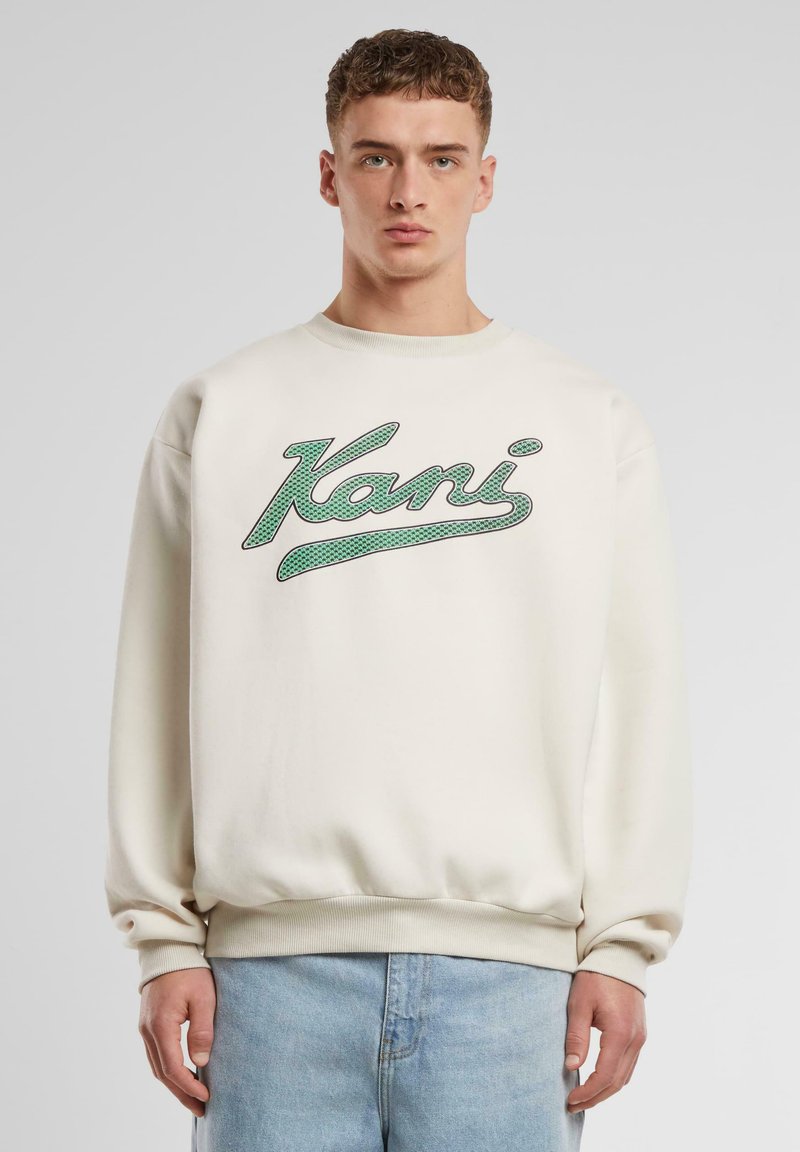 Creme sweatshirt med grøn "Kani" logo, ribbede manchetter og talje. Casual pasform med glat tekstur og blødt materiale. Matchet med lyseblå jeans.